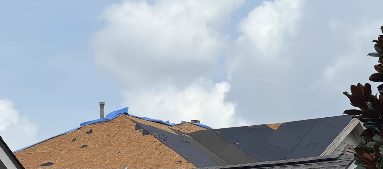 Roof replacement in progress: one slope stripped to the wooden decking while new shingles go on the adjacent slope