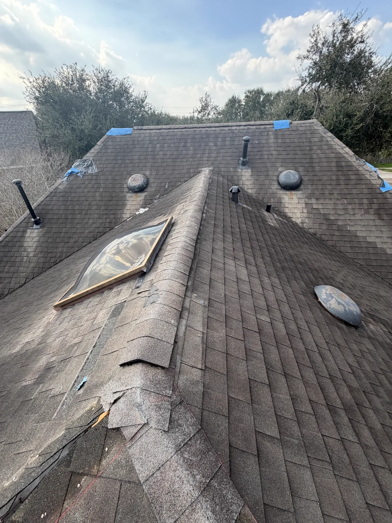 Roof inspection with damage marked in blue tape near a skylight