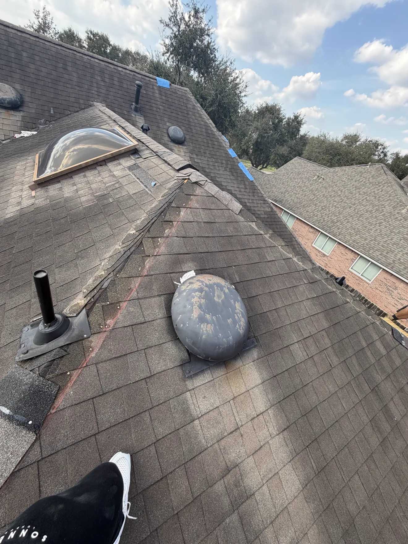 Storm damage marked with blue tape on a shingle roof