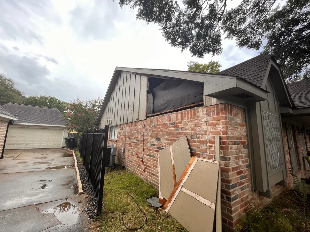 Gable end with damaged siding panels removed and stacked, weather barrier exposed