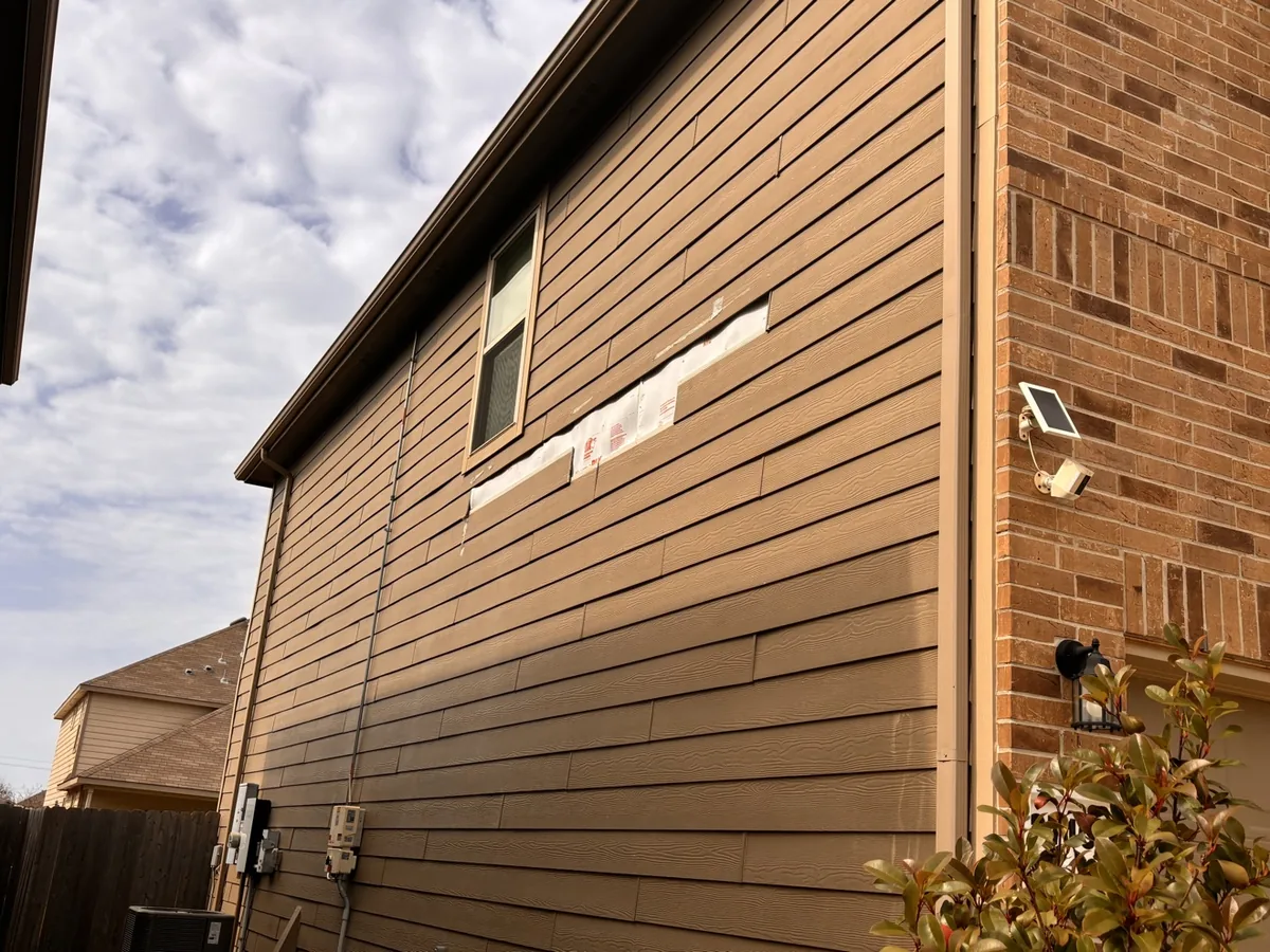 Damaged fiber-cement siding boards with the weather barrier exposed underneath